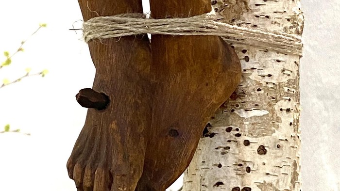 Ein hölzerner Arm ist an einem Birkenstamm festgebunden.