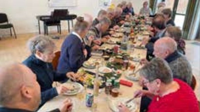 En gruppe ældre folk sidder til middag på lang bord.