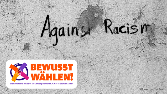 „Anti-Rassismus-Botschaft auf Betonwand mit der Aufschrift *BEWUSST WÄHLEN!* – darunter das Logo der katholischen Initiative.“