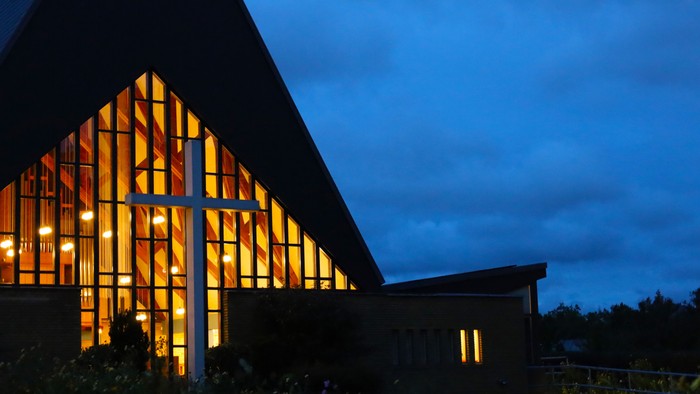 En moderne bygning med store glassvinduer, belyset fra inden for ved daggry.