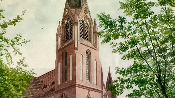 Gotische Kirche mit hohem Turm, eingerahmt von üppigen grünen Bäumen unter bewölktem Himmel.