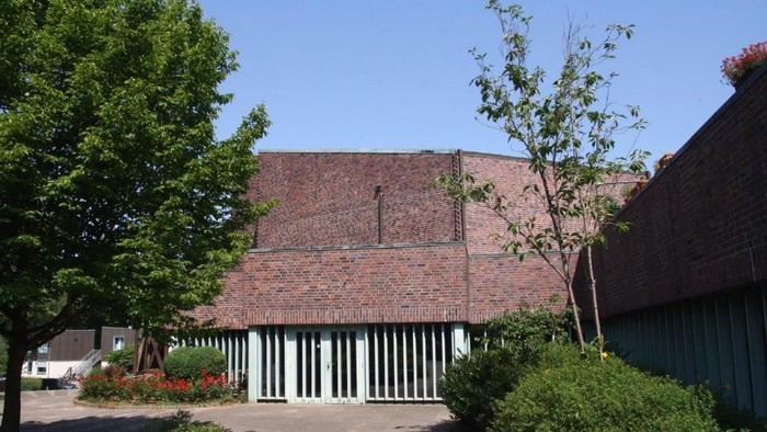 Modernes Ziegelgebäude mit grünen Garagentoren, umgeben von Grünflächen und Bäumen unter klarem Himmel.