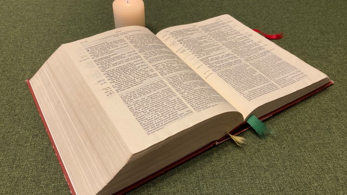 Offenes Buch mit brennender Kerze darauf auf grüner Oberfläche