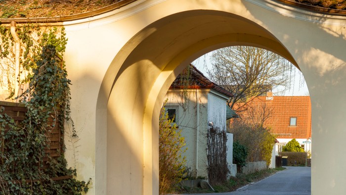 Ein charmanter bogenförmiger Durchgang führt durch einen malerischen, efeubewachsenen Eingang zu einer ruhigen Wohnstraße.