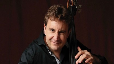 En mand smiler, mens han spiller på en kontrabas i et svagt oplyst miljø.