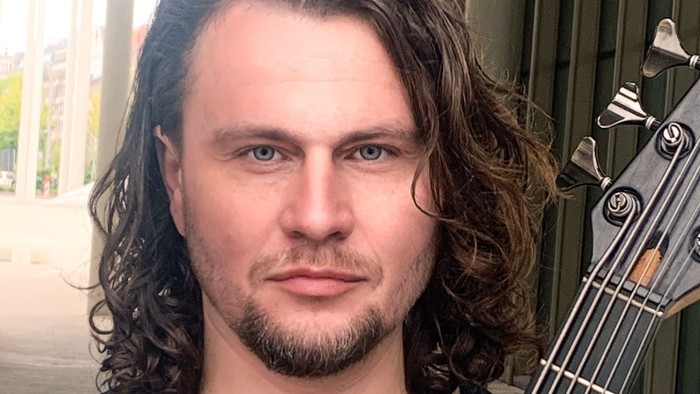 Ein Mann mit langen Haaren und Bart, der im Freien einen Kontrabass hält.