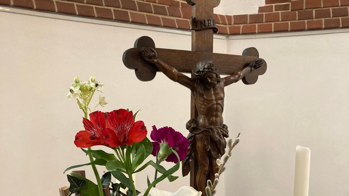 Ein Kreuz mit Jesusfigur, ein Blumenstrauß und eine aufgeschlagene Bibel