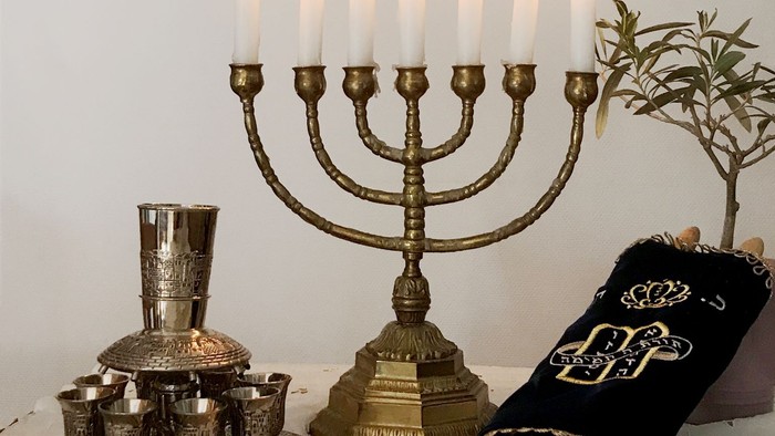 Ein goldener Menorah mit brennenden Kerzen, eine silberne Kiddusch-Tasse, ein schwarzes Tzedakah-Box und ein offener Sefer Torah auf einem Tisch