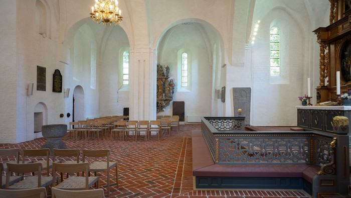Elegant kirkeinteriør med træbænke, buede vinduer og et centralt alterområde.