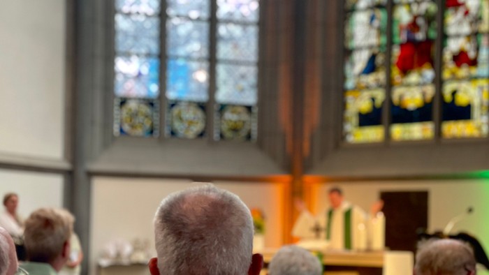 Kirchengemeinde feiert Gottesdienst, bunte Fenster, Menschen beten