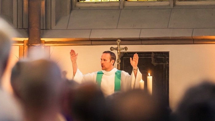 Ein Priester steht in einer Kirche und hält die Hände erhoben.