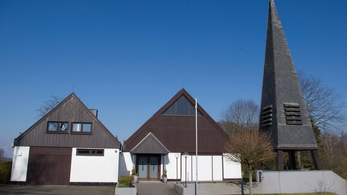 Moderner Bau mit dreieckigen Dächern und hohem Turmspitz unter klarem, blauem Himmel.