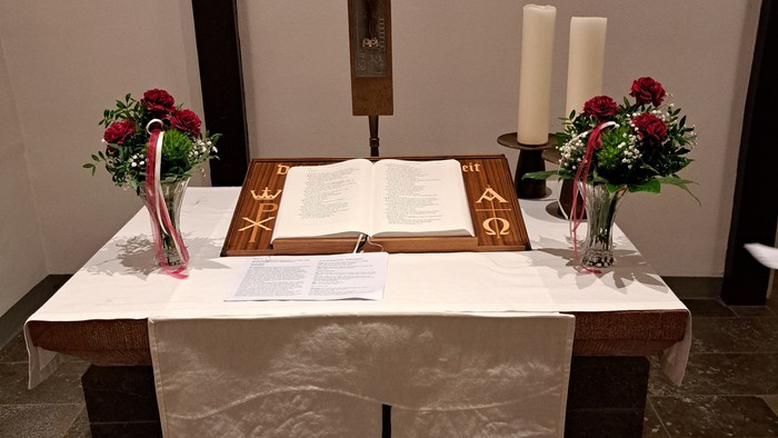 Elegante Altaraufstellung mit einem Kreuz, einem aufgeschlagenen Buch, Kerzen und Blumendekorationen auf einem bedeckten Tisch.