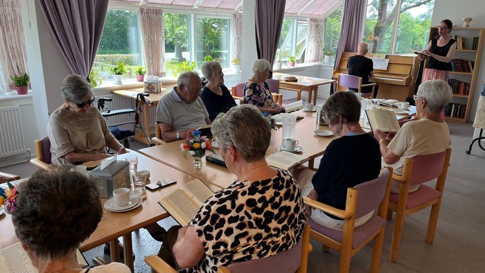 En gruppe ældre mennesker samlet omkring borde i et veloplyst rum, optaget af forskellige aktiviteter.