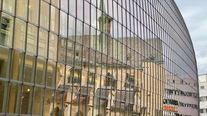 Glasfassade eines modernen Gebäudes mit Spiegelung eines historischen Gebäudes.