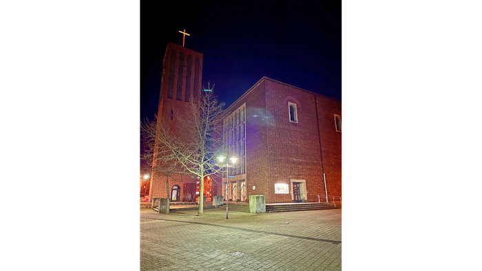 Kirchengrundstück bei Nacht mit beleuchtetem Kreuz und Laternen