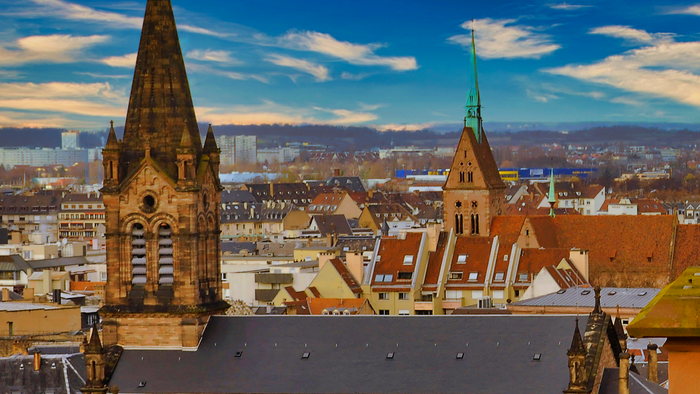 Paysage urbain historique européen mettant en valeur des églises médiévales et des toits sous un ciel bleu vibrant.
