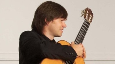 Eine Person, die lächelnd eine hellfarbige klassische Gitarre spielt.