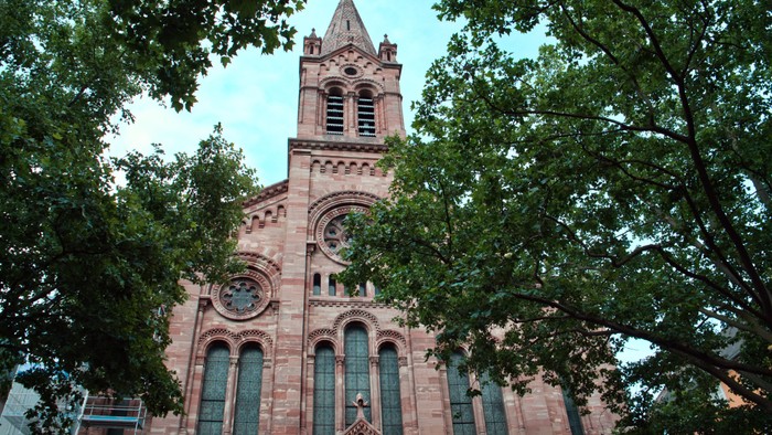 Une église en brique avec un clocher, entourée d'arbres verts.