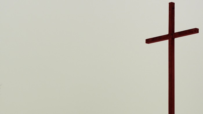 Ein einsames Kreuz ragt schroff vor dem Hintergrund eines hellen, bewölkten Himmels auf.