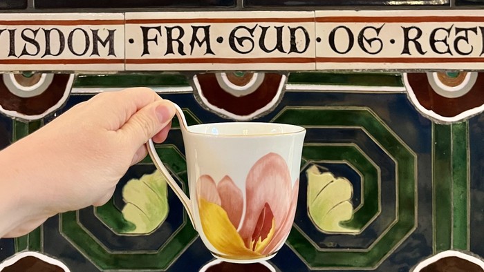 Hånd holder en teglæber med blomster i en dekoreret rum