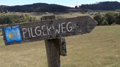 Holzschild mit Pilgerweg Richtungspfeil in ländlicher Umgebung
