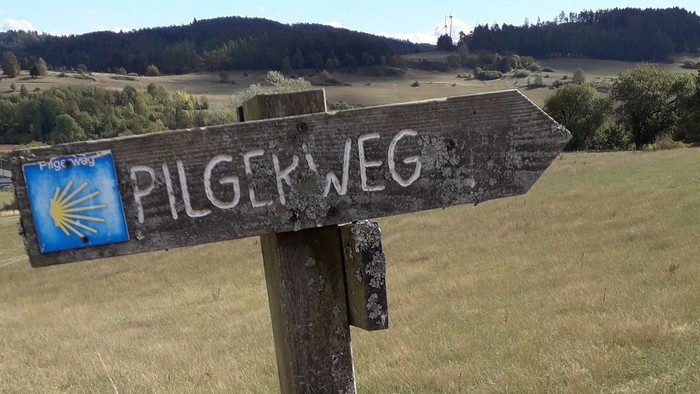 Holzschild mit Pilgerweg Richtungspfeil in ländlicher Umgebung