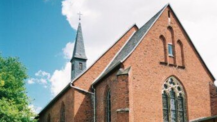 Ein rotes Backsteingebäude mit spitzen Fenstern und einem Turm, umgeben von grünem Gras und Blumen.