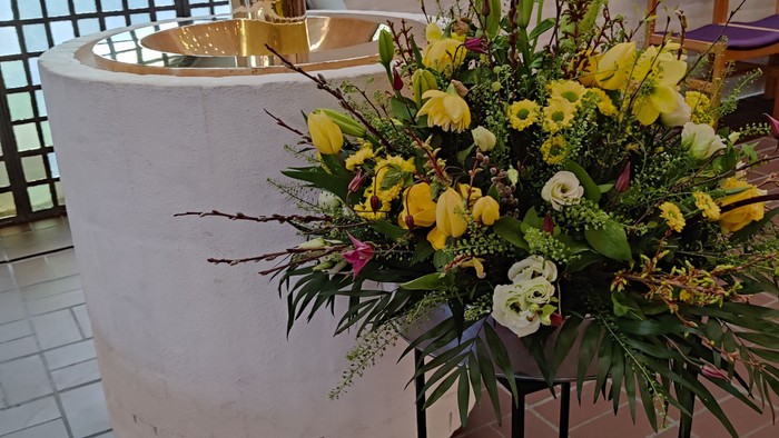 En stor blomsterarrangement med gule og hvide blomster står på en stativ foran en fontæne.