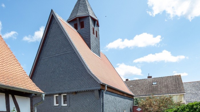 Graues Haus mit rotem Dach und Glockenturm unter blauem Himmel.