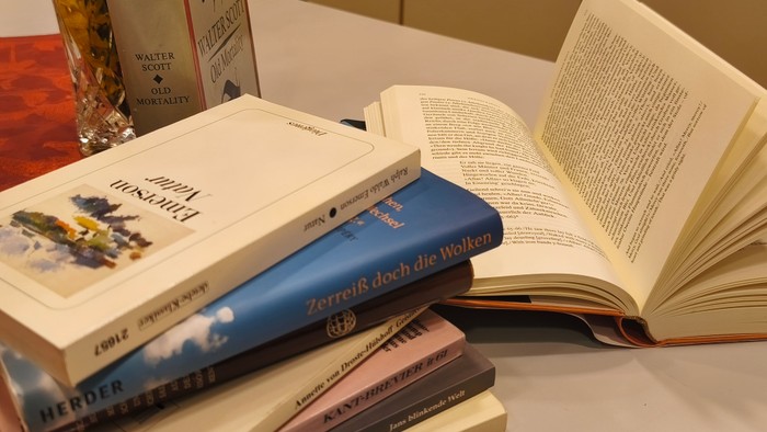 Eine Sammlung offener und geschlossener Bücher, die auf einem Tisch angeordnet sind, mit einem Glasgetränkebehälter in der Nähe.