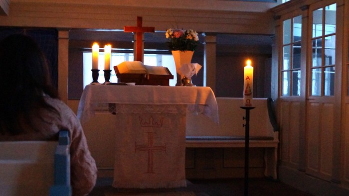 Ein friedvoller Kirchenaltar, erleuchtet von Kerzen, mit Blumenarrangements und einem Kreuz in einem schwach beleuchteten Raum.