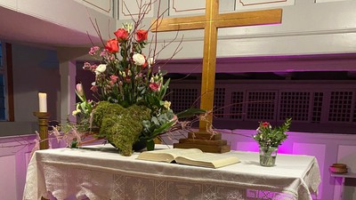 Eleganter Altar, geschmückt mit Blumen, Kerzen und rosafarbenen herzförmigen Ballons unter einem hölzernen Kreuz.