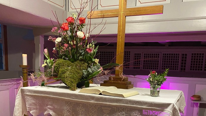 Eleganter Altar, geschmückt mit Blumen, Kerzen und rosafarbenen herzförmigen Ballons unter einem hölzernen Kreuz.