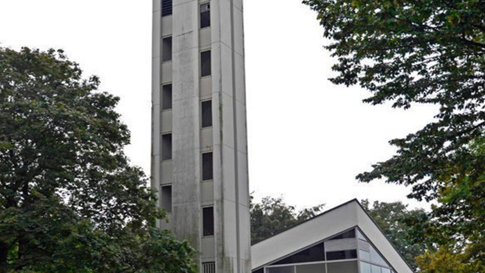 Das Bild zeigt eine moderne Kirche mit hohem Turm und Glasfront, umgeben von Bäumen.