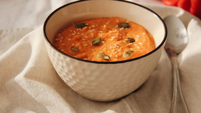 En lille bol med soppe og en ladel på et hvidt tørklæde ved siden af en pumpa og løv.