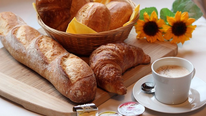 Ein Frühstücksbrett mit Croissants, Baguette, Kaffee und Blumen
