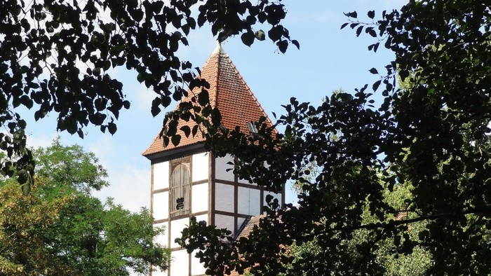 Hinter Bäumen verbirgt sich ein hübsches, altes Haus mit spitzem Dach.