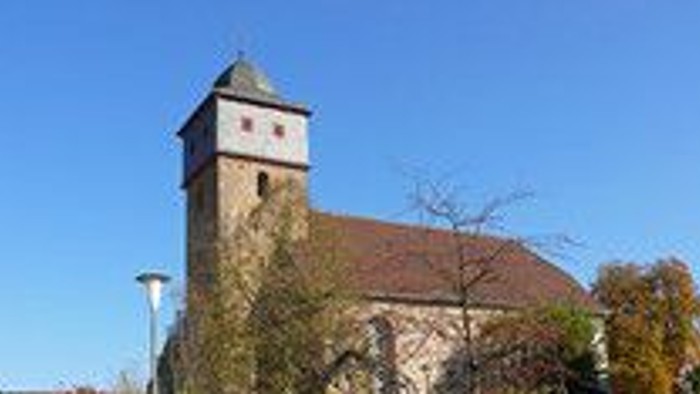 Historische Kirche mit hohem Glockenturm vor klarem blauem Himmel und herbstlichem Laub.