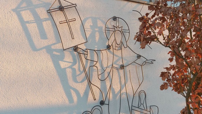 Dekorative Metallskulptur, die kunstvolle Schatten religiöser Figuren und Laternen an eine Wand wirft.