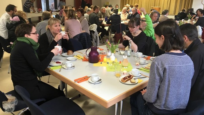 Eine Gruppe von Menschen sitzt an Tischen und isst gemeinsam in einem Raum.