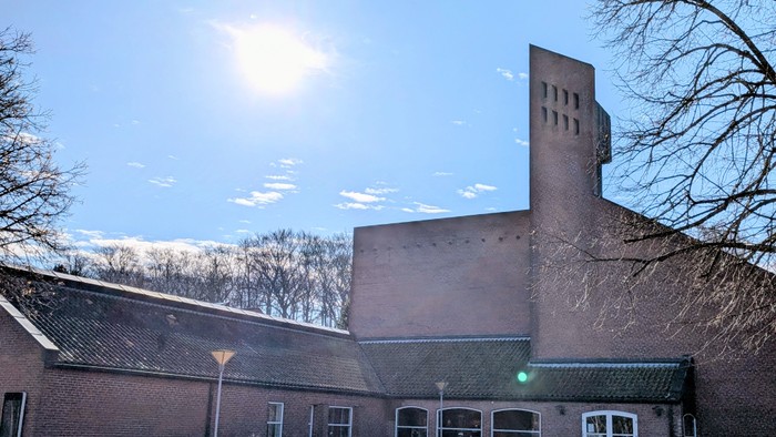 Moderne murstensbygning med en høj skorstenslignende struktur under en klar blå himmel.
