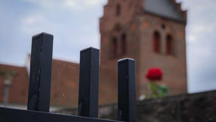 Tre sort stænger foran mursten og kirke med blomst.