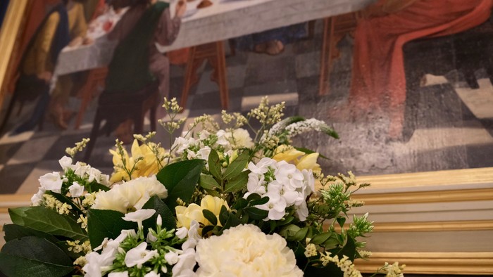 En blomsterstok med hvide og gule blomster foran et maleri af en kirkeinterior.
