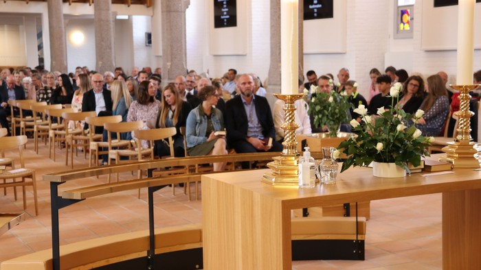 En kirke med en stor samling af mennesker, der sidder på bænke.