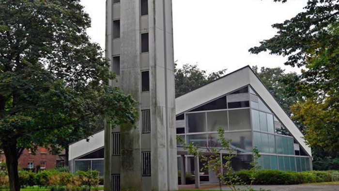 Das Bild zeigt eine moderne Kirche mit hohem Turm und Glasfront, umgeben von Bäumen.