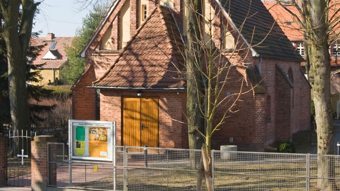 Historische Backsteinkirche mit steilem Satteldach und Holztür, umgeben von kahlen Bäumen.
