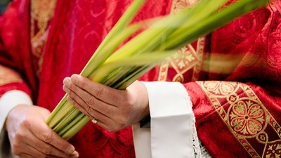 Eine Person in zeremonieller Robe hält Palmzweige, wahrscheinlich während einer religiösen Prozession.