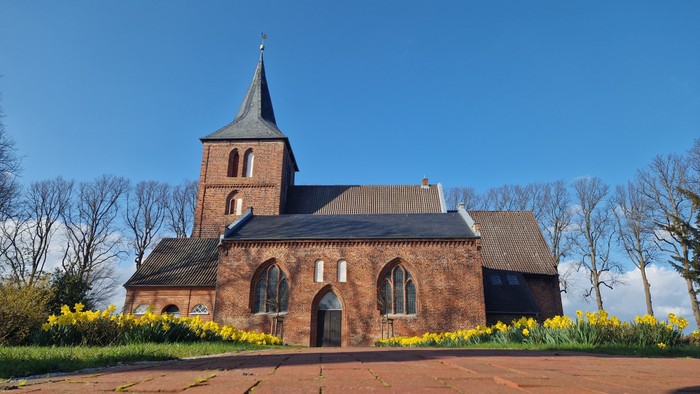 Ein rotes Backsteingebäude mit spitzem Turm und gelben Blumen im Vordergrund