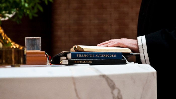 En person i religiøst tøj åbner en ritualbog med titlen *